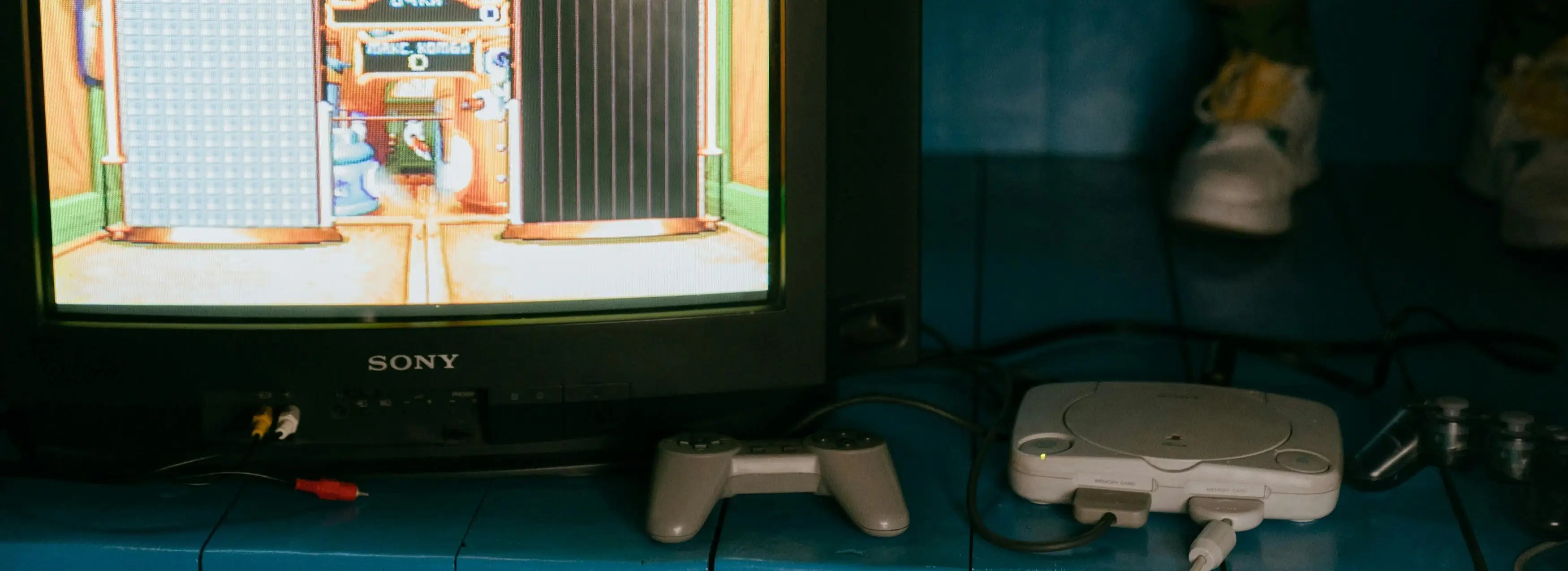 Vintage Sony television displaying a video game with gaming console and controller on a blue surface.